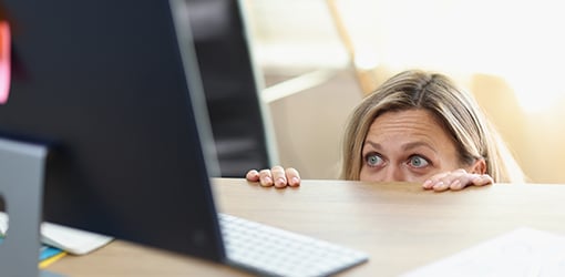 Pöydän alle piiloutunut henkilö katsoo kauhuissaan tietokoneensa näyttöä.