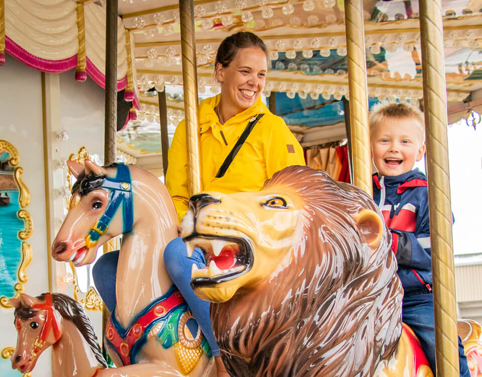 An adult and a child laughing together on a carousel ride.