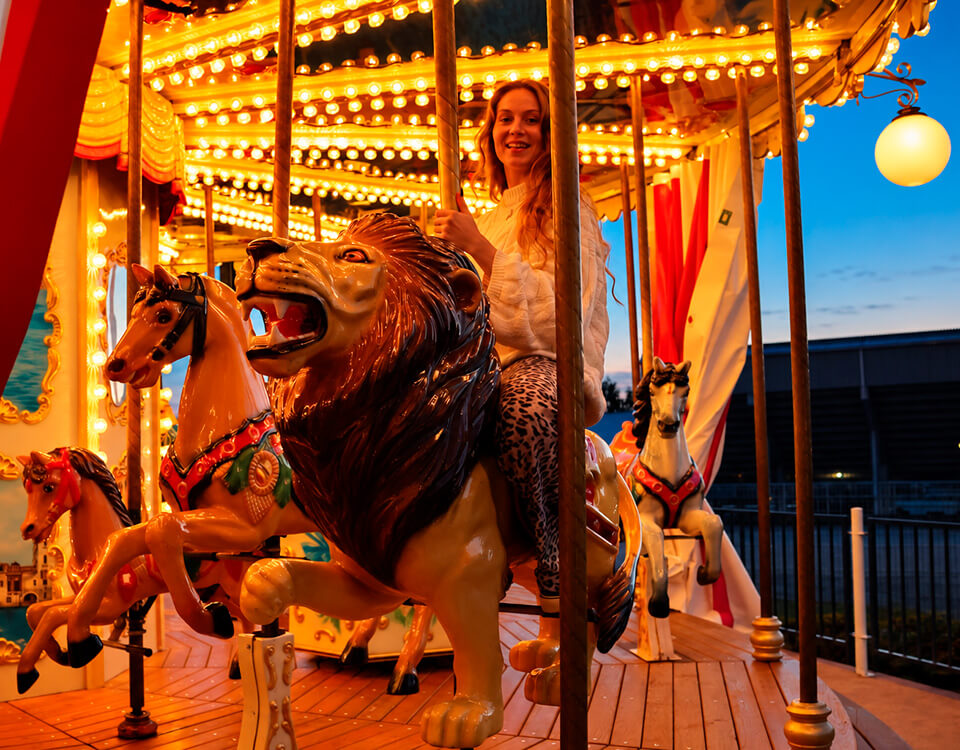 A smiling visitor enjoying a carousel ride at PowerPark as evening falls.