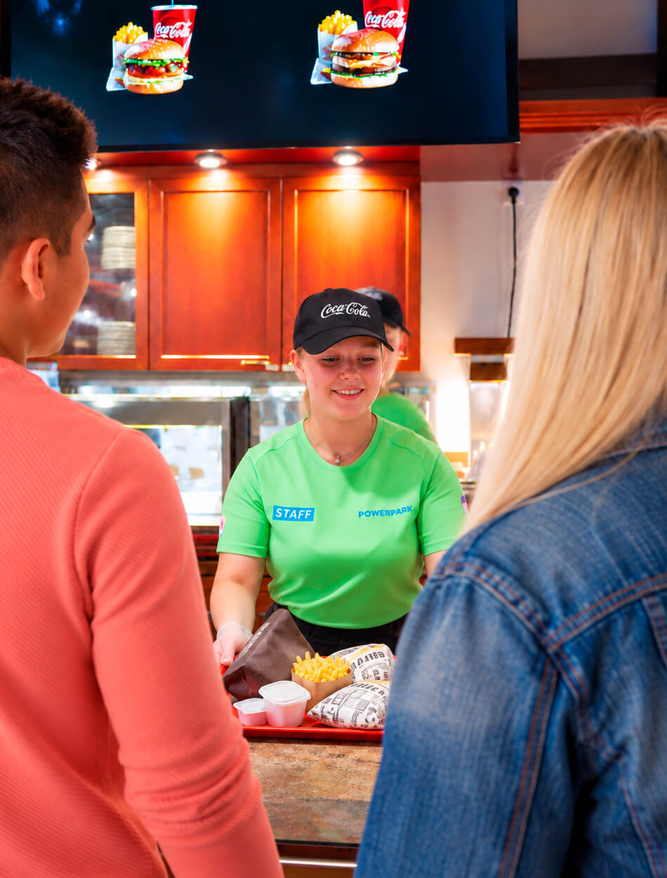 A display indicates that the food is ready as a smiling staff member hands a tray of food to customers.