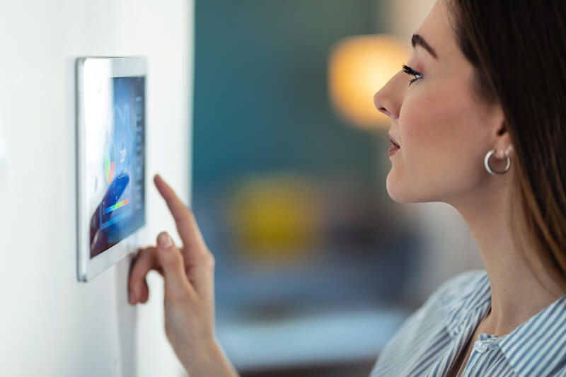 A woman adjusts her home settings using a tablet mounted on the wall.