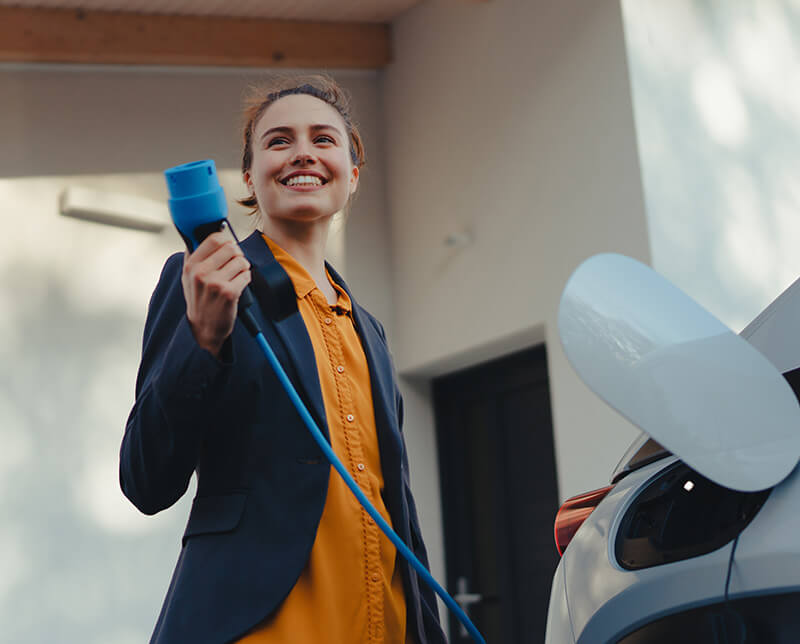 Nainen lataa sähköautoaan kotona. Nykyaikaiset energiajärjestelmät mahdollistavat joustavuuden, kestävän kehityksen ja uusien teknologioiden saumattoman integroinnin.
