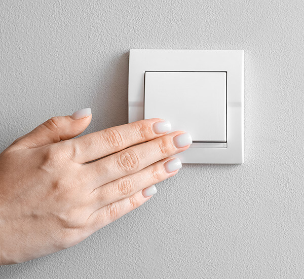 Käsi koskettaa valokatkaisijaa kuvaten toimivan sähkönjakelun tärkeyttä.