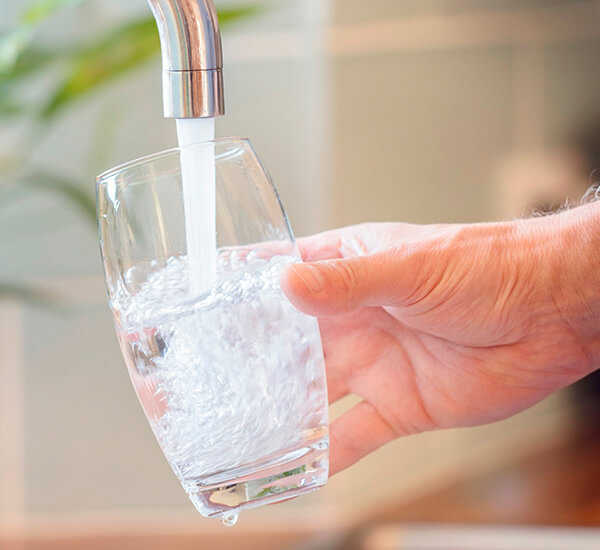 A person filling a glass with water from a kitchen tap.