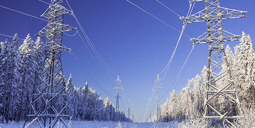 Sähkölinjaa lumisen metsän keskellä auringonpaisteisena pakkaspäivänä.