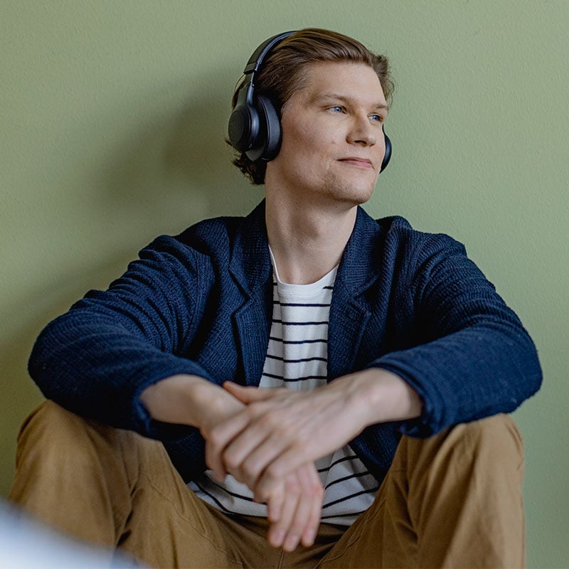 The trainee sits on the floor leaning against the wall and listens to the work meeting with headphones