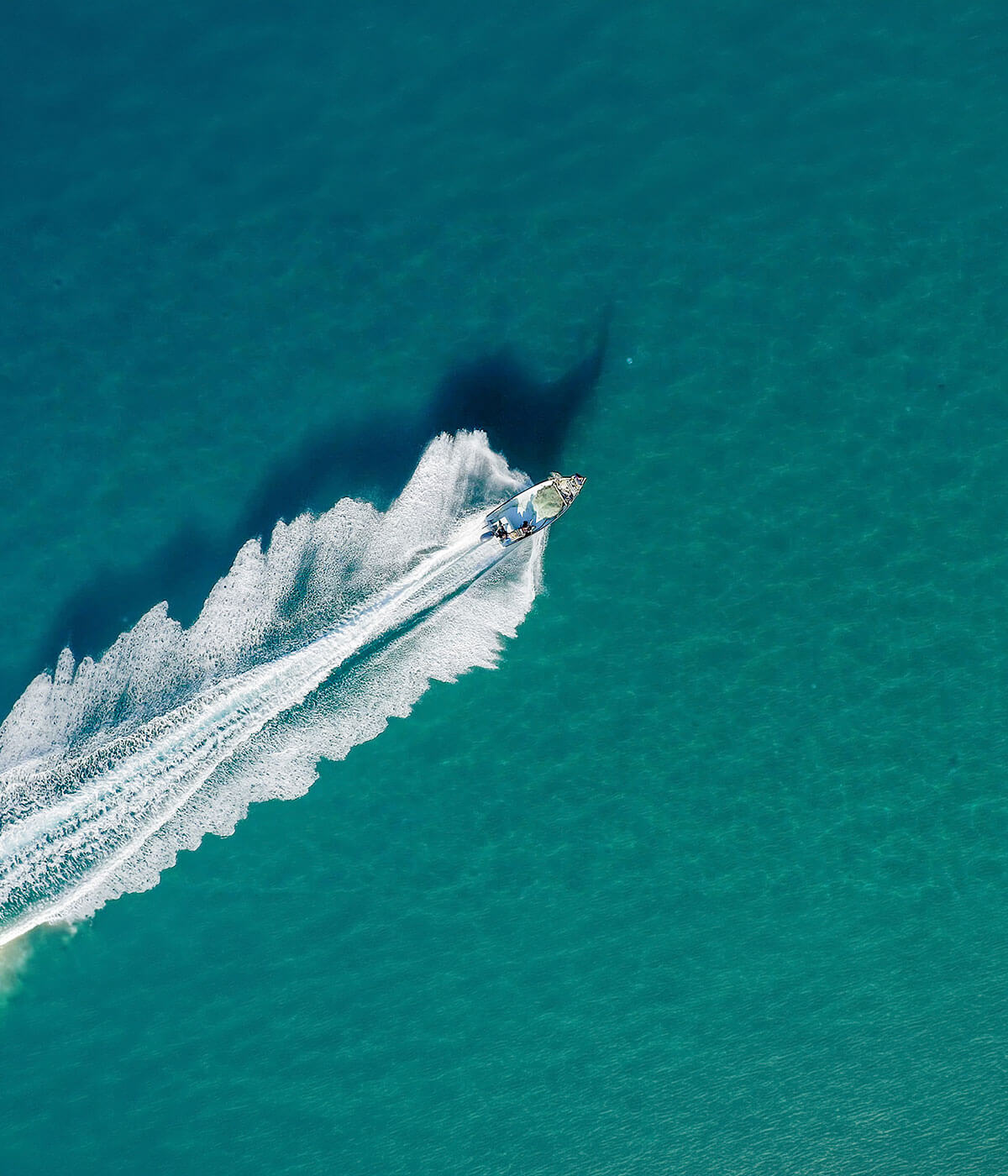 Aerial view of a speedboat cutting through turquoise open water, leaving a wide white wake trailing behind it.