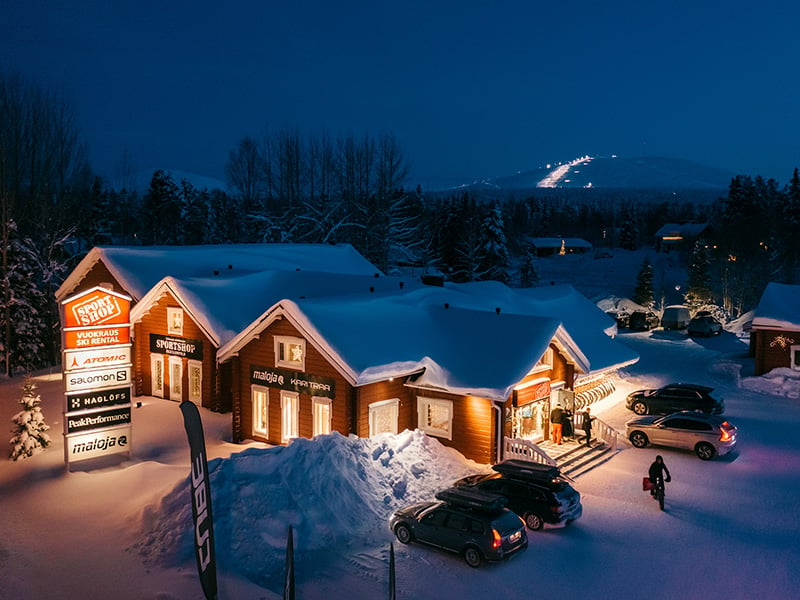 The exterior of Äkäslompolo Sportshop's store in the evening lighting, Ylläs mountain can be seen in the background.