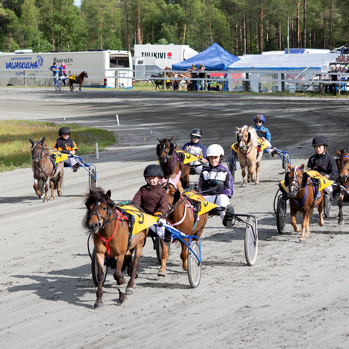 Poneja juoksemassa raviradalla, taustalla Valjaskulman varusteauto