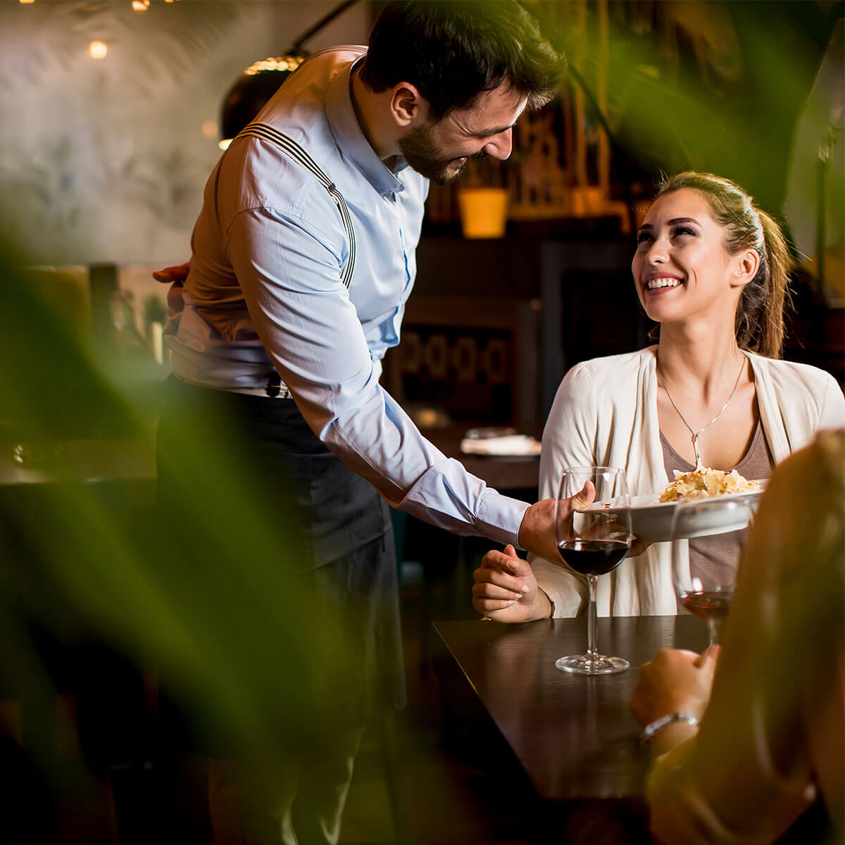 Two women having dinner at a restaurant with male waiter next to their table serving a dish