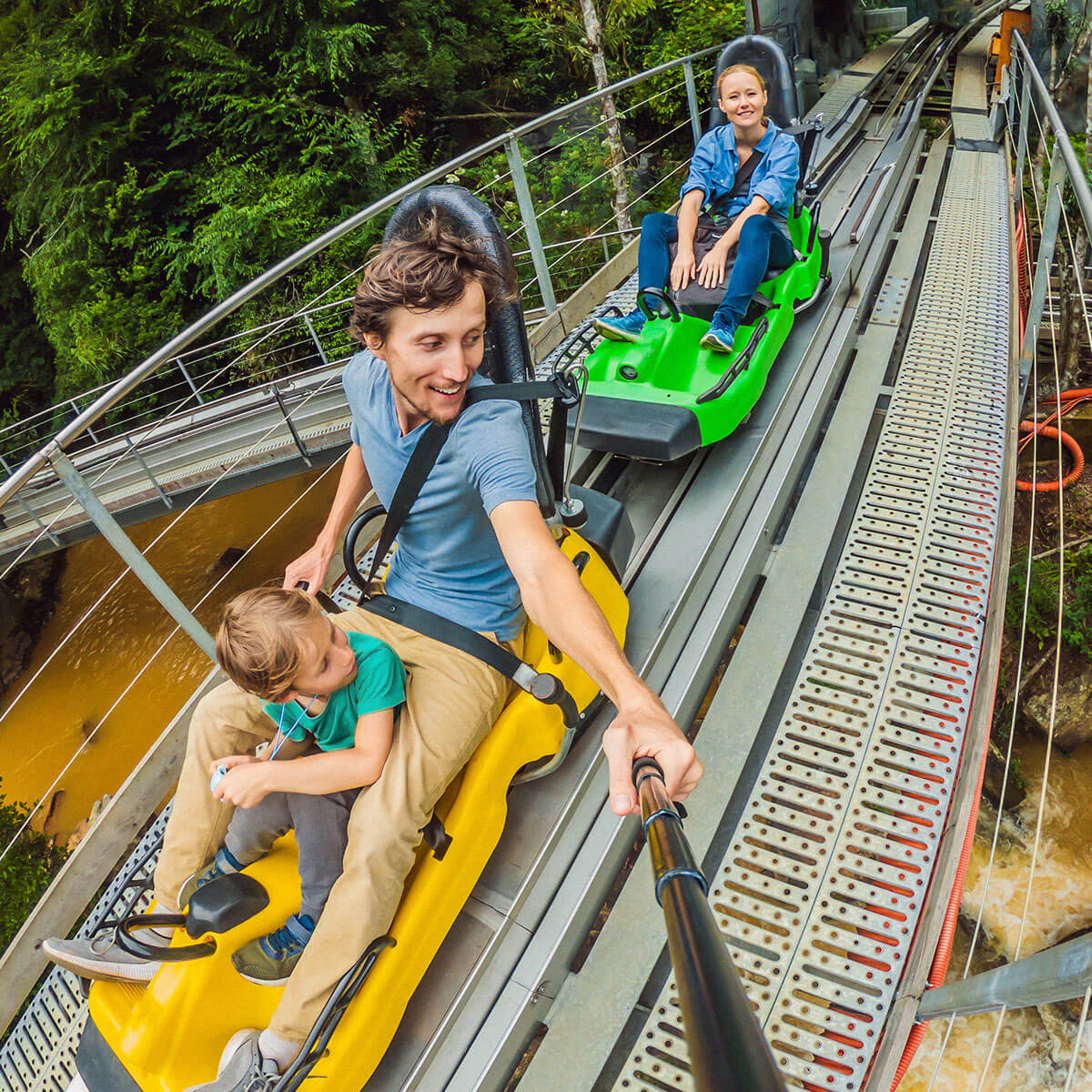 Family of three in theme park ride and father taking a photograph with selfie stick