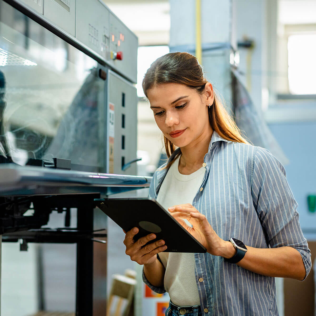 Female professional using a tablet in an industrial setting, accessing unified data and connected systems