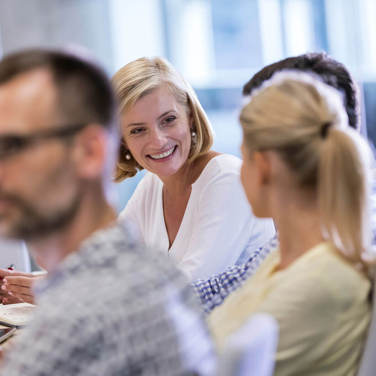 Hymyilevä asiantuntija keskustelee tiimin kanssa työpajassa, jossa keskitytään palvelun personointiin ja asiakaslähtöiseen kehittämiseen.