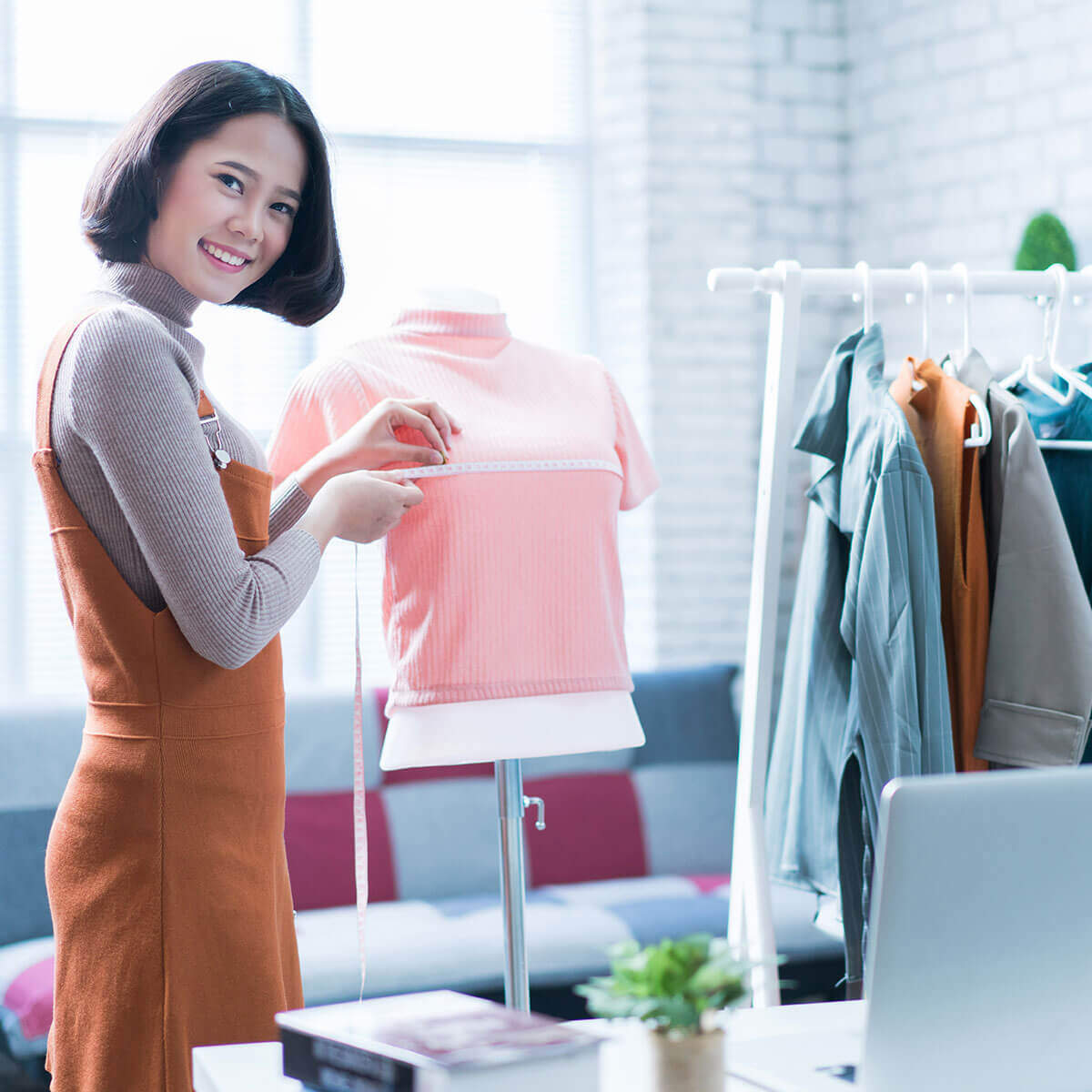 A smiling clothing store owner is measuring a pink sweater on a fitting mannequin.