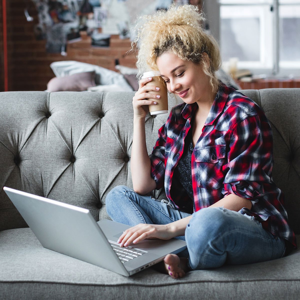 En ung rutete kvinne som sitter på en sofa og handler på nettet