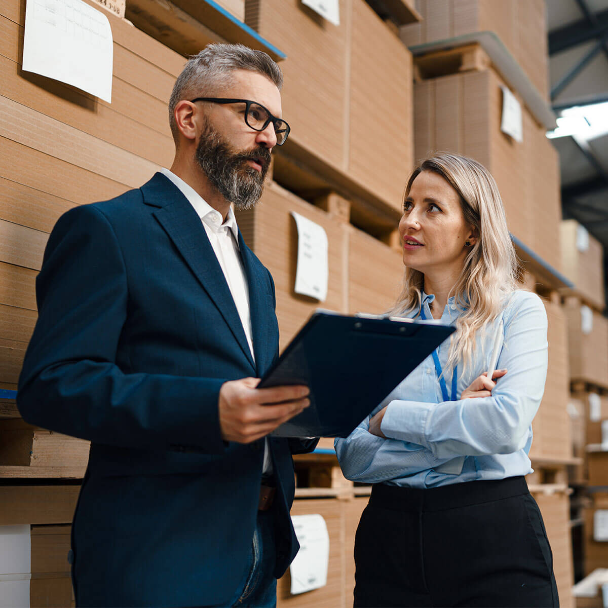 Two professionals discussing operations in a warehouse surrounded by stacked cardboard boxes