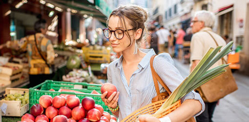 Woman selecting apples at outdoor market. Market sellers use mobile POS system by Solteq Commerce Cloud.