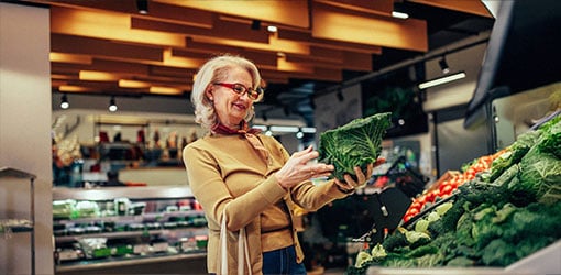 En kvinna i en beige tröja undersöker kål i frukt- och grönsaksavdelningen i en livsmedelsbutik