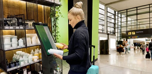 A blonde woman paying for her purchases at a self-service checkout at an airport store.