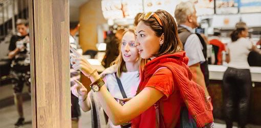 Two female friends making order with self-service kiosk at a restaurant