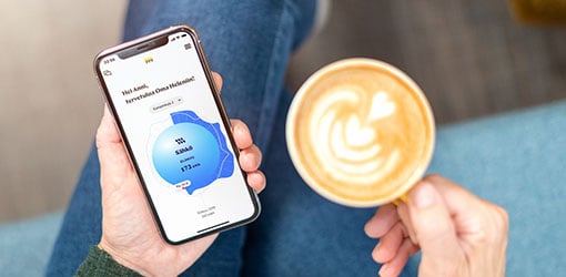 Asiakas tarkastelee tietojaan Helenin onlinesta kotisohvallaan kahvikuppi kädessä