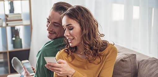 Satisfied customers are smiling and sitting on their couch reading a message from their electricity company that offers tips for reducing electricity consumption.
