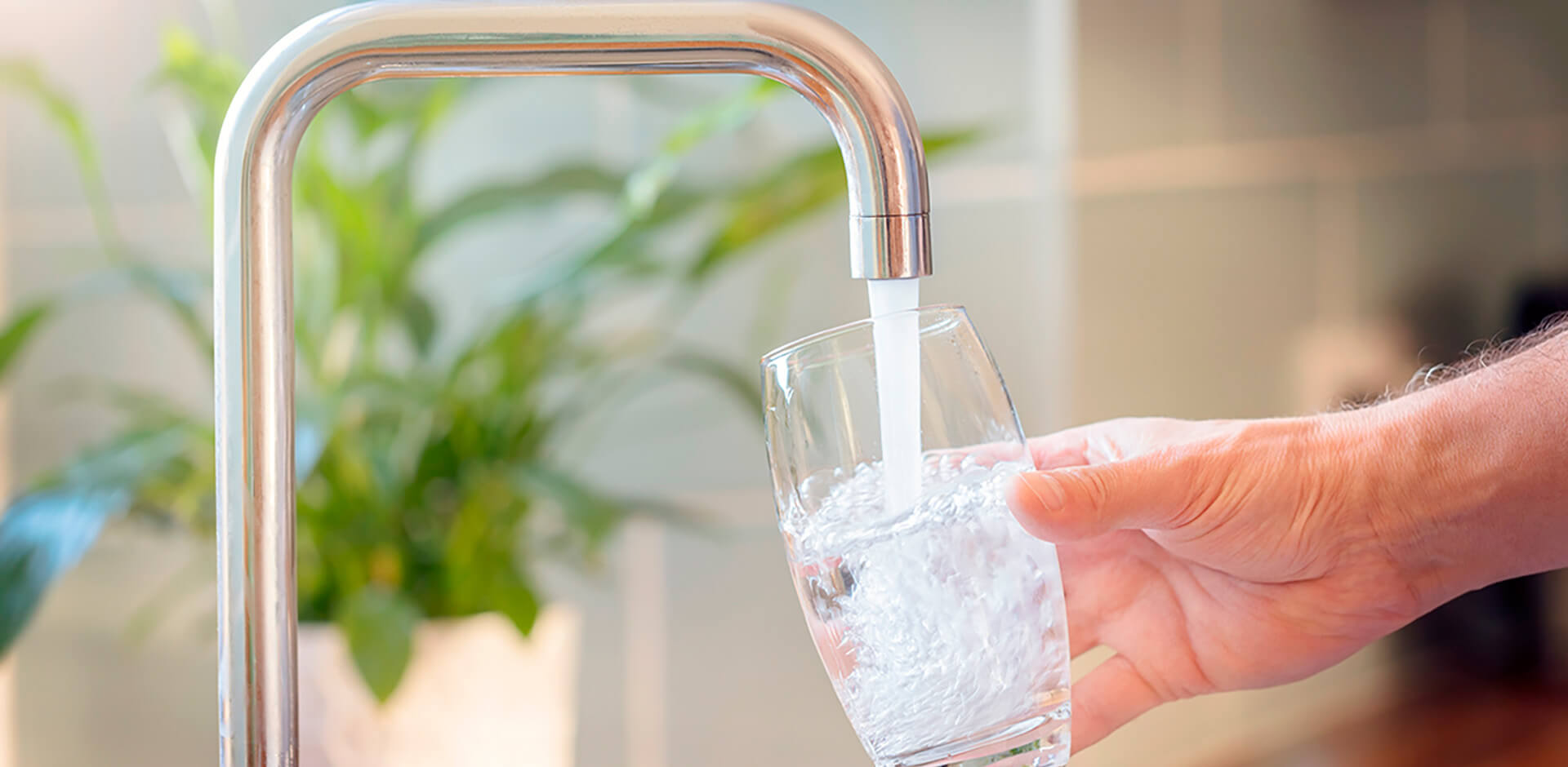 A person pours water into a glass from the kitchen tap.