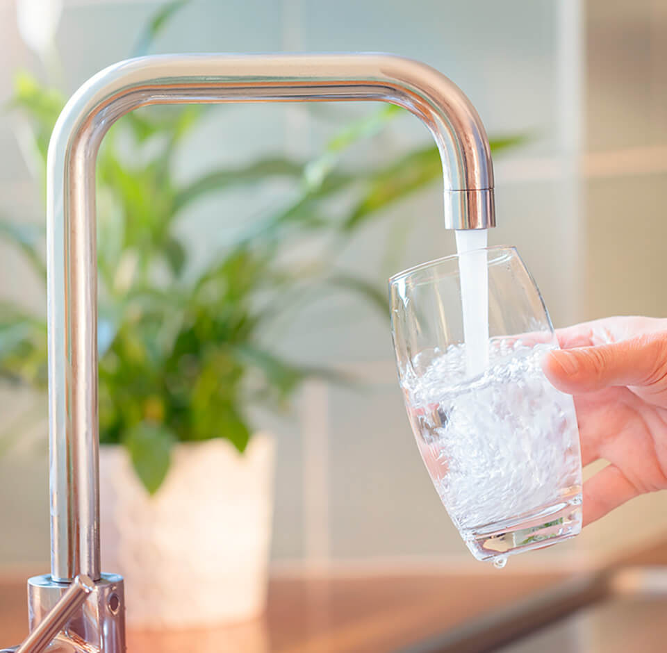 Henkilö ottaa juotavaa keittiön hanasta.