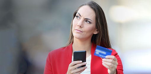 Mietteliäs punatakkinen ja tummahiuksinen nainen pohtii luottokortti ja puhelin kädessä verkkokaupan ongelmakohtia