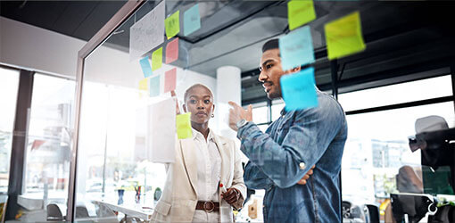 Woman and man looking at Composable Commerce plan from post-its' on a glass wall