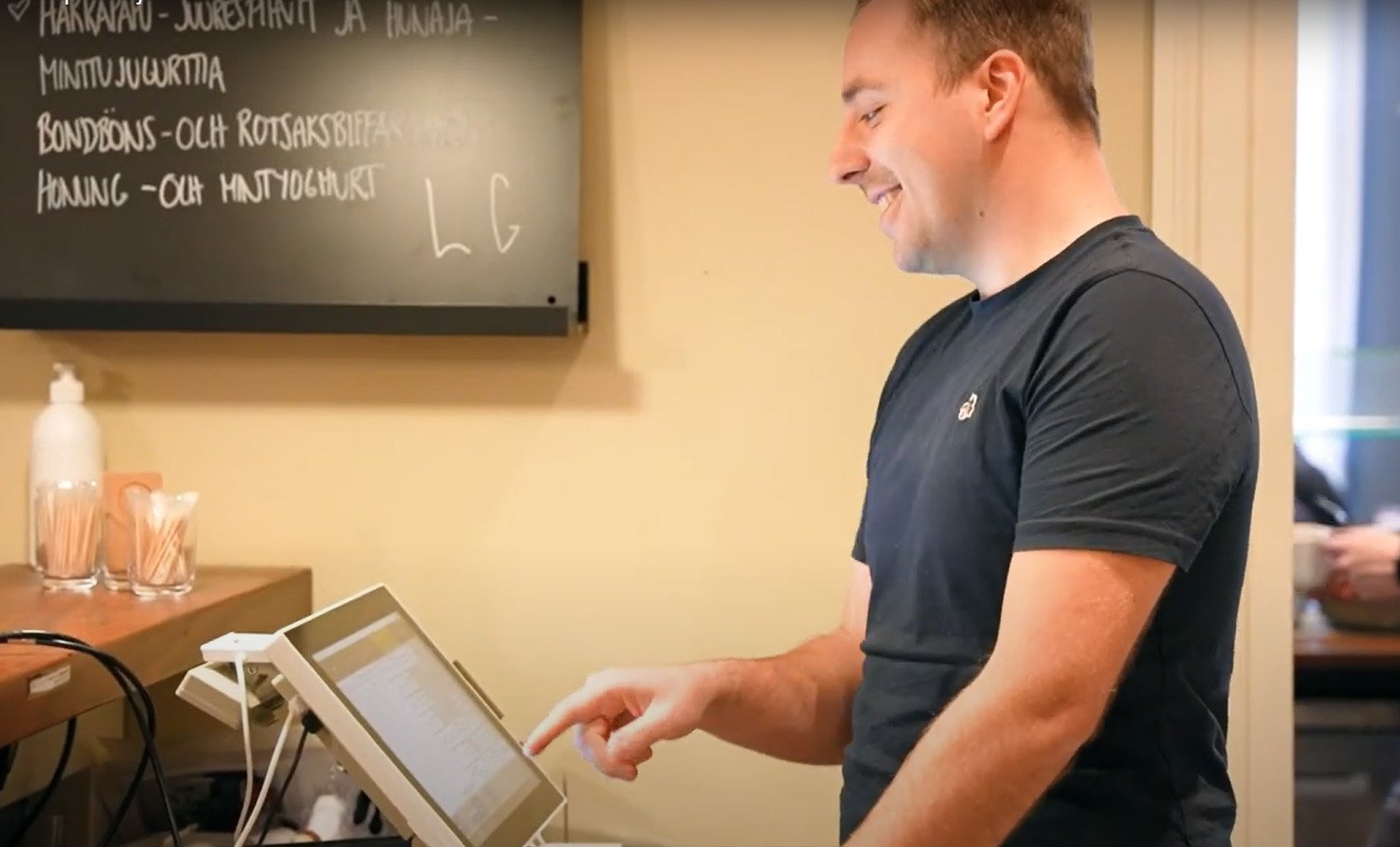 Joona Terävä, System Specialist, VoiVeljet is using POS device behind the counter in a restaurant.