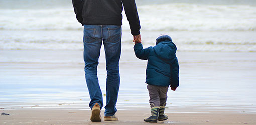 Aikuinen pitää lasta kädestä kun he seisovat rannalla