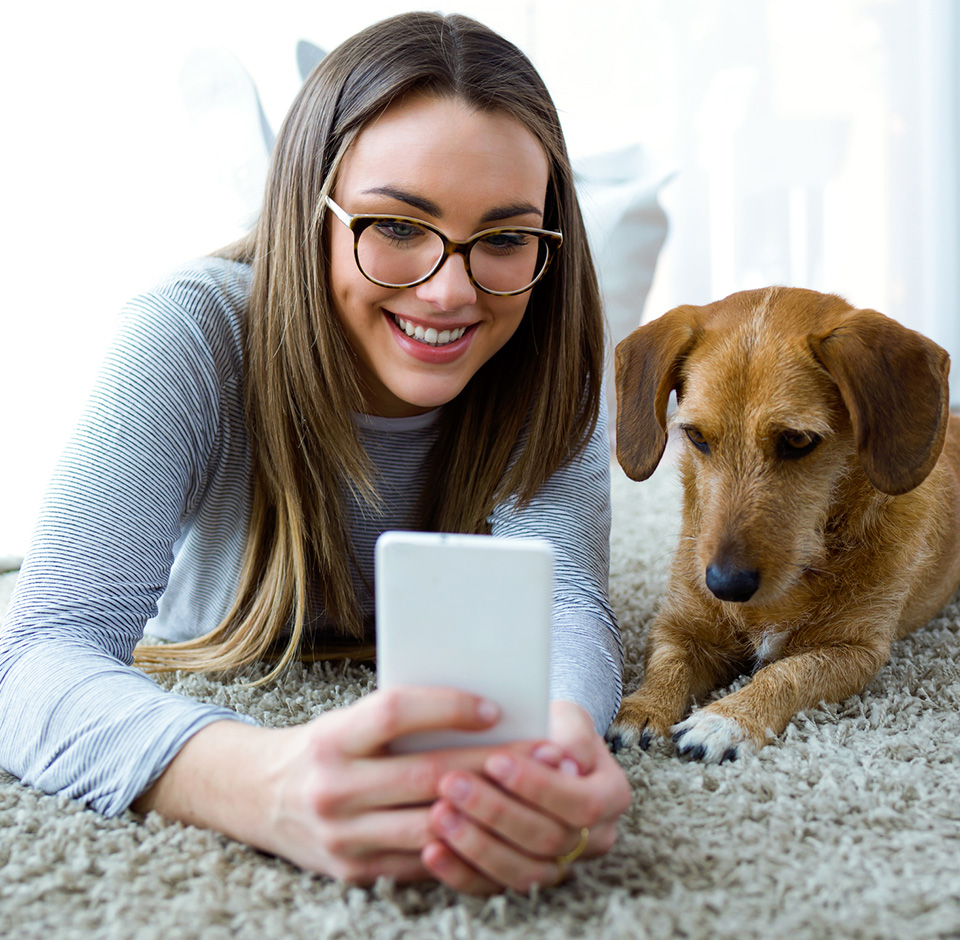 Nainen makaa lattialla koiran vieressä ja katsoon kännykkään tullutta viestiä.