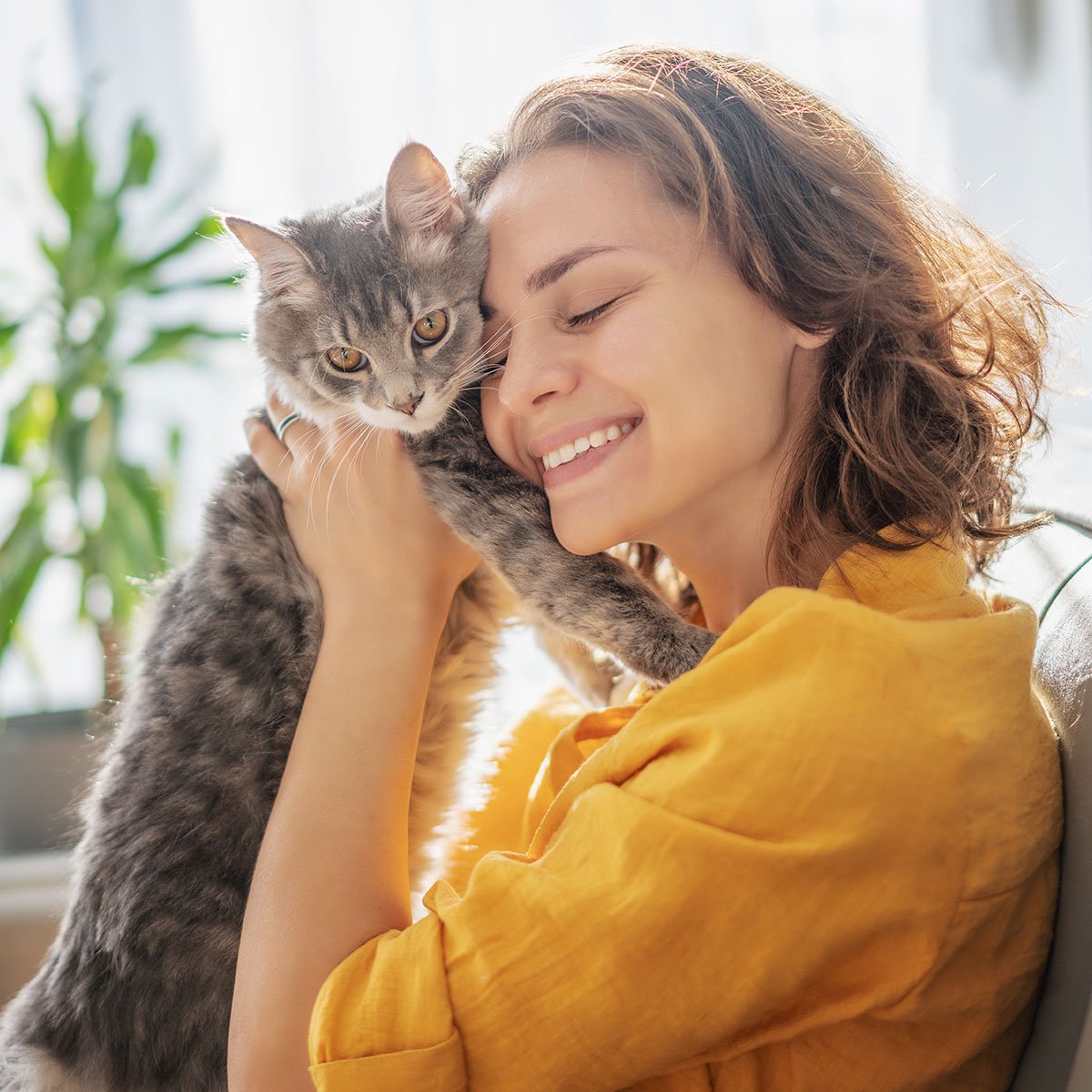 En smilende kvinde i en gul skjorte holder en kat i sine arme