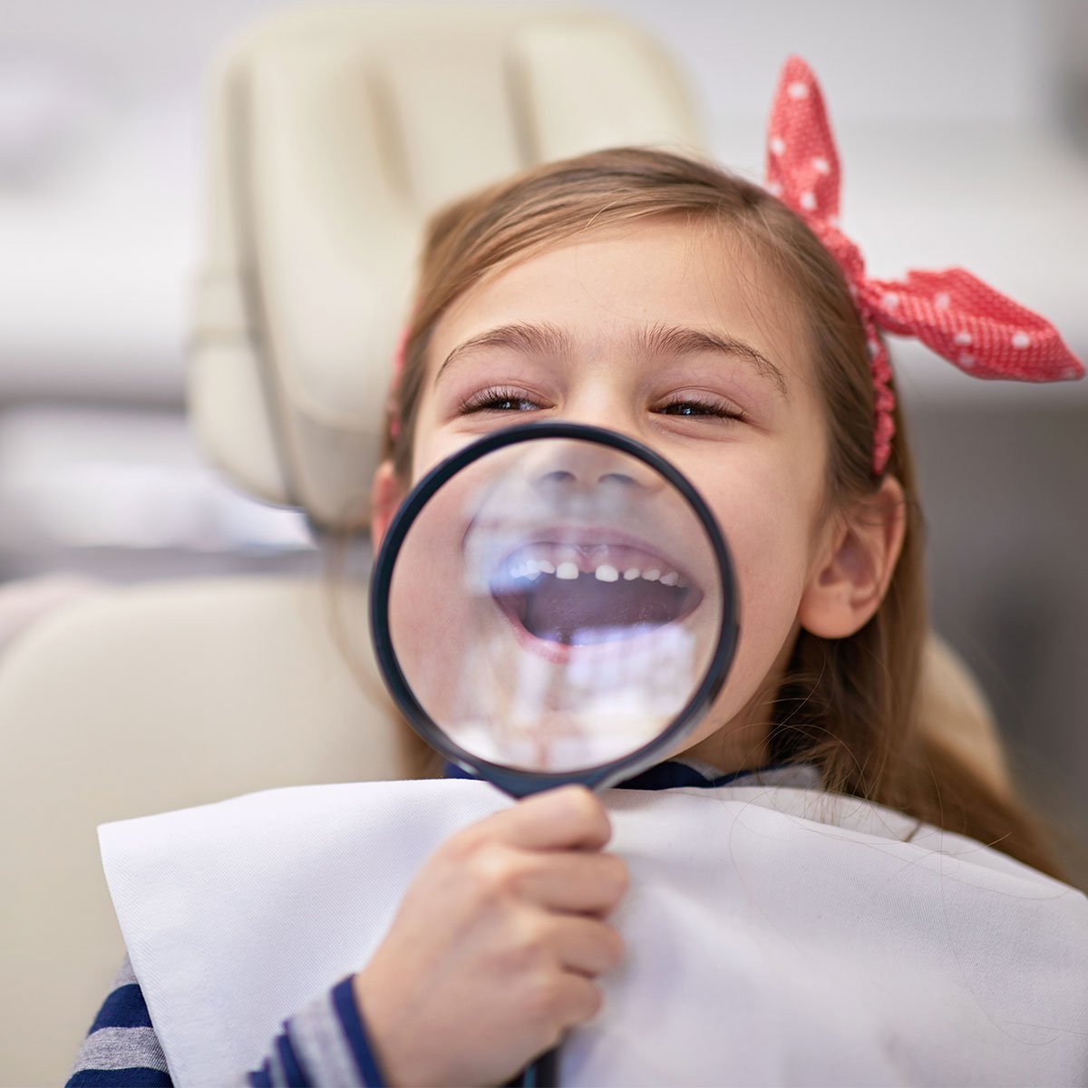 Pige med et forstørrelsesglas på en tandlæge stol