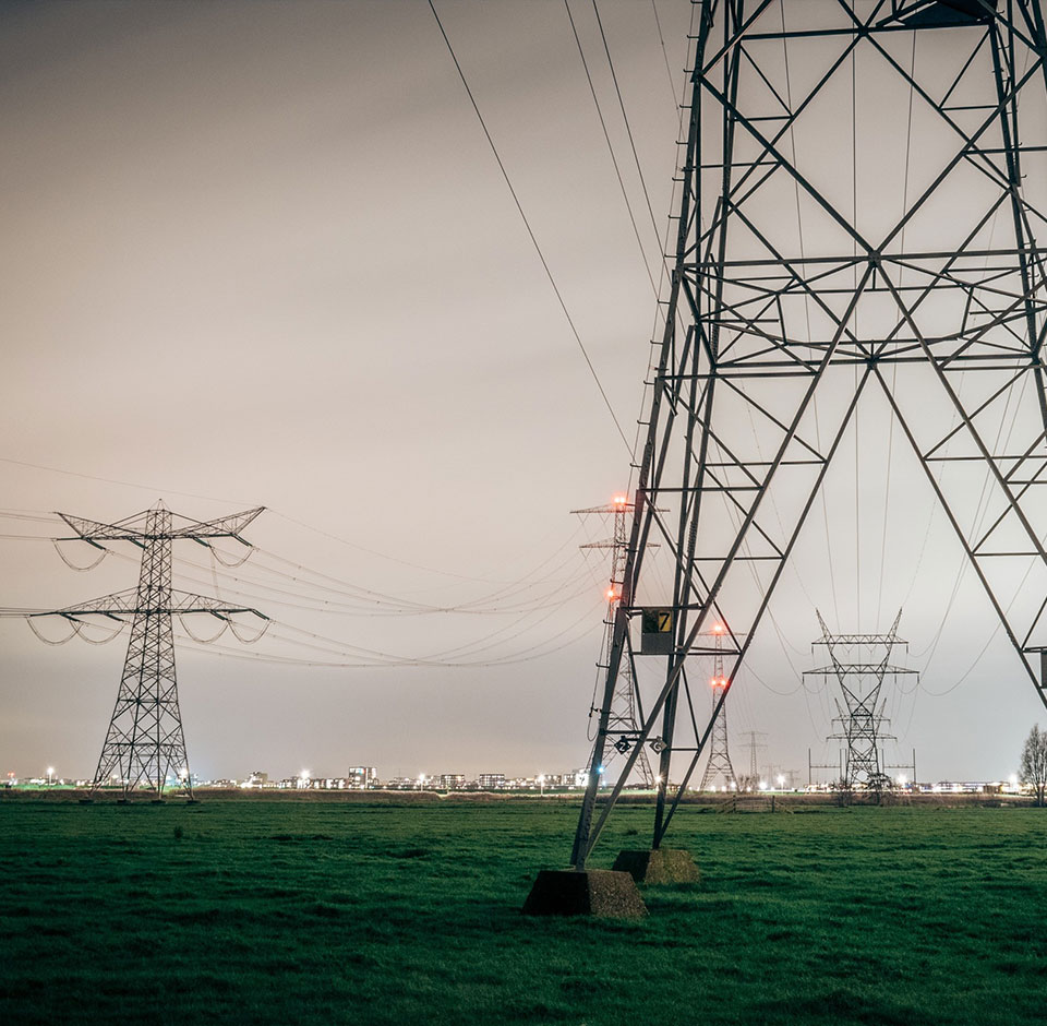 Solteq Utilities CIS - Kraftledninger på tværs af græsbane med bysilhouet i baggrunden