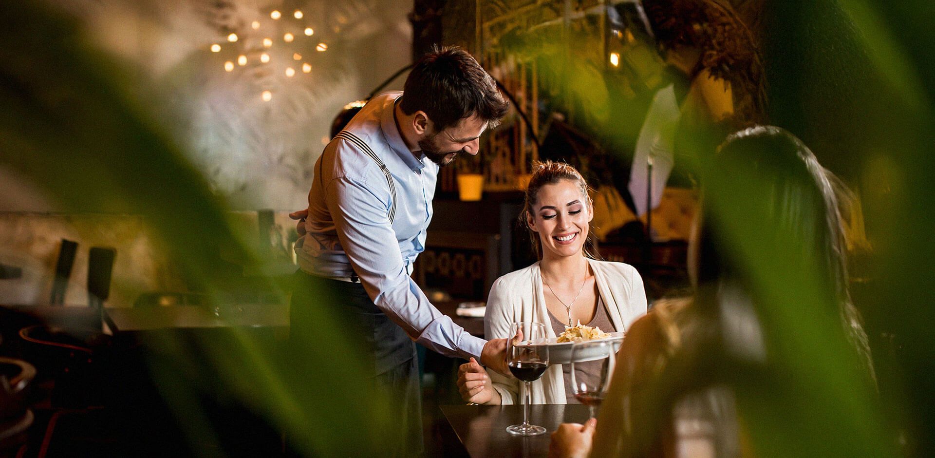 Male waiter serving dinner to a female customer at a restaurant that is operated by Solteq Commerce Cloud point-of-sale system