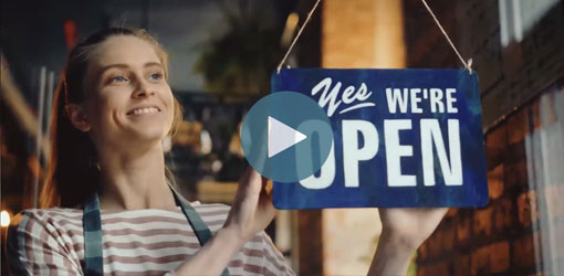 Kuvakaappaus Solteq Commerce Cloud esittelyvideosta - nainen avaamassa ravintolaa ja kääntää Open kylttiä.