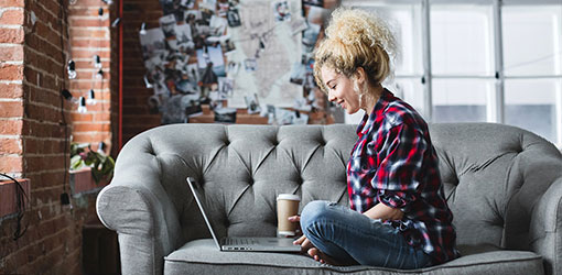 Ung kvinne sitter på en sofa i loftsleiligheten og handler på nett i e-handel