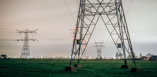 Solteq Utilities CIS - Kraftledninger på tværs af græsbane med bysilhouet i baggrunden