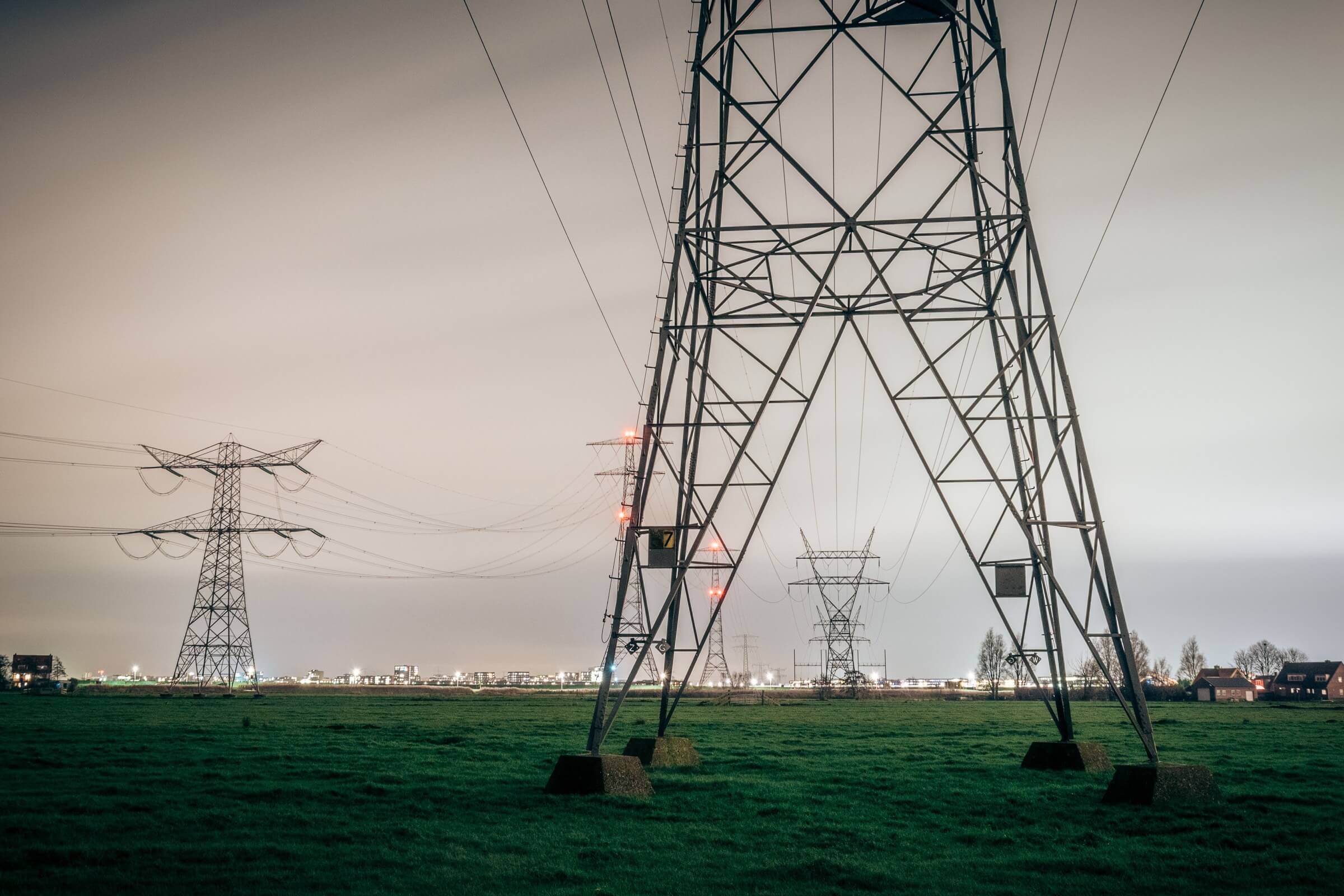 Powerlines accross grass field with city silhouette in the background.